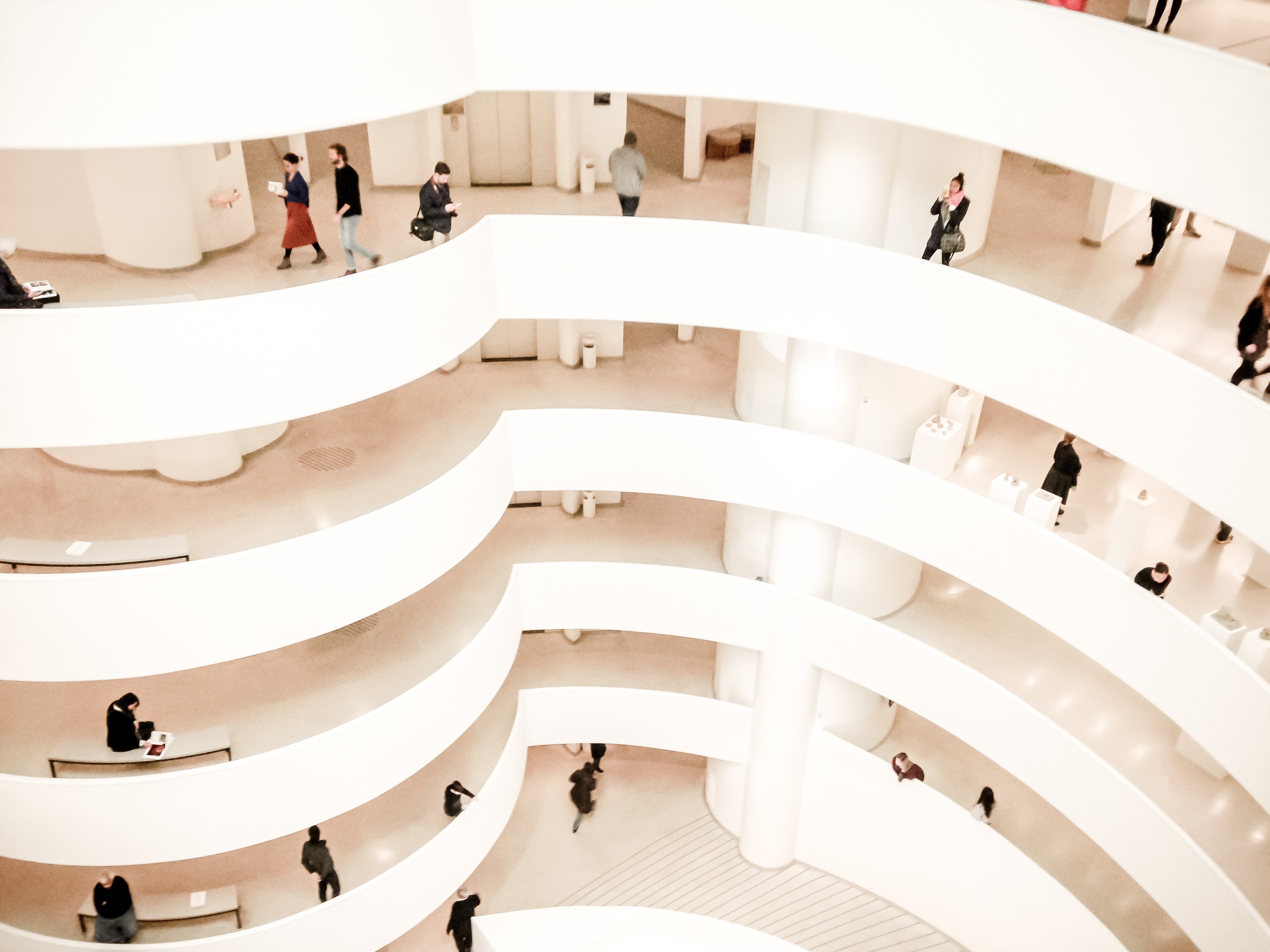 An image from above of nested white levels of the inside of a building with people in them