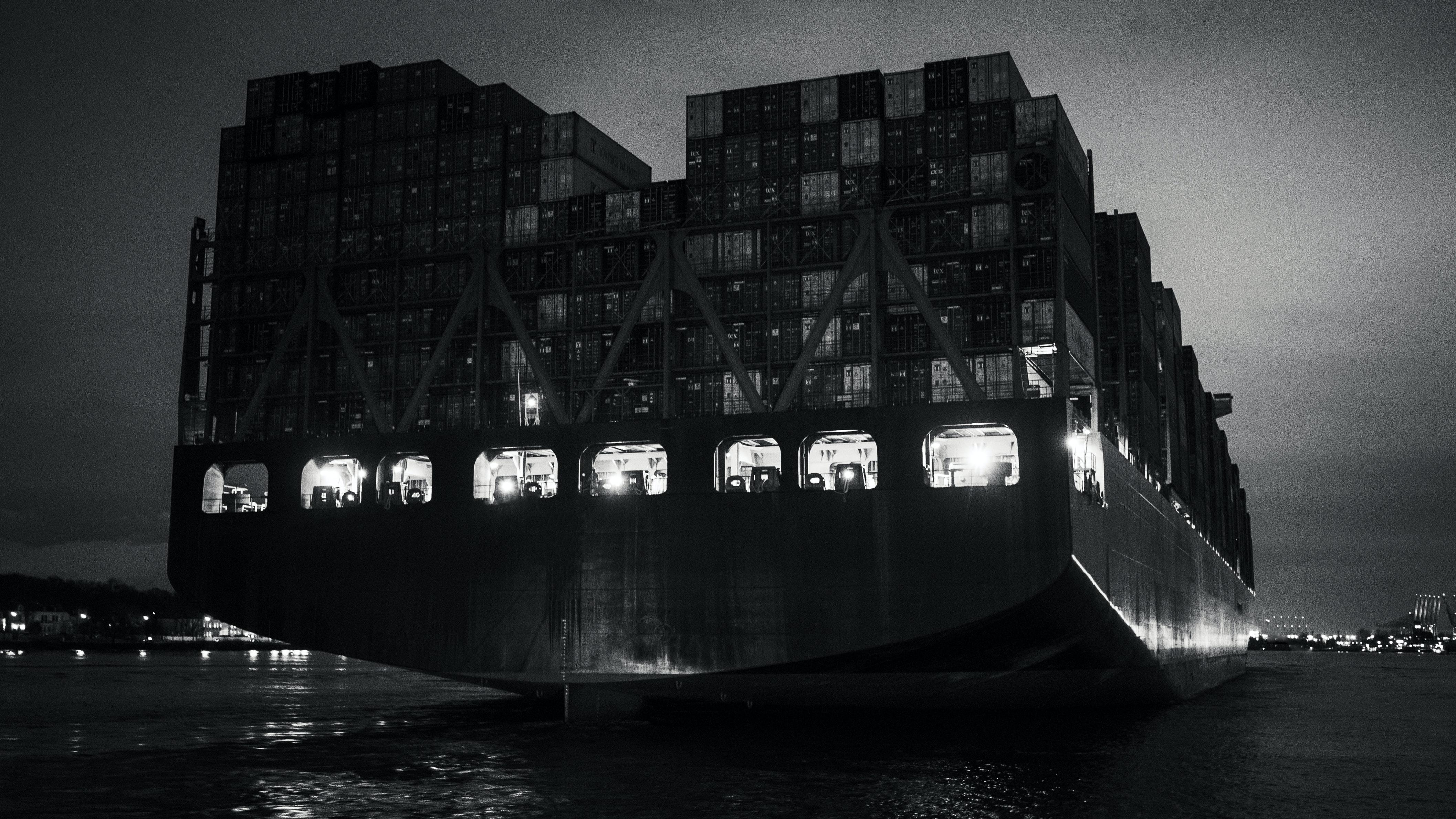 A black and white image of a container ship, viewed from the rear.