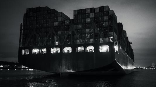 A black and white image of a container ship, viewed from the rear