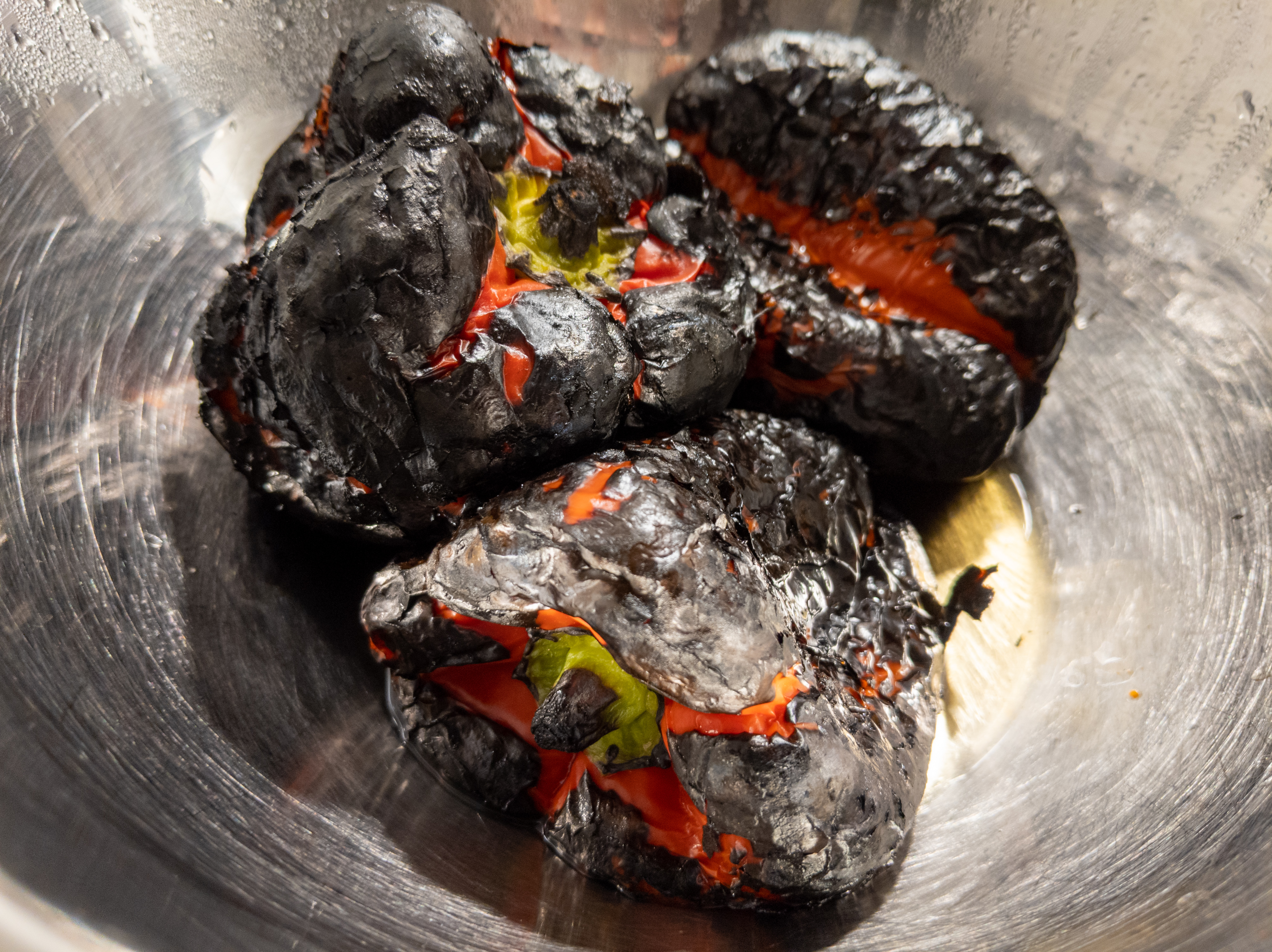 A metal bowl with whole, blackened peppers in it
