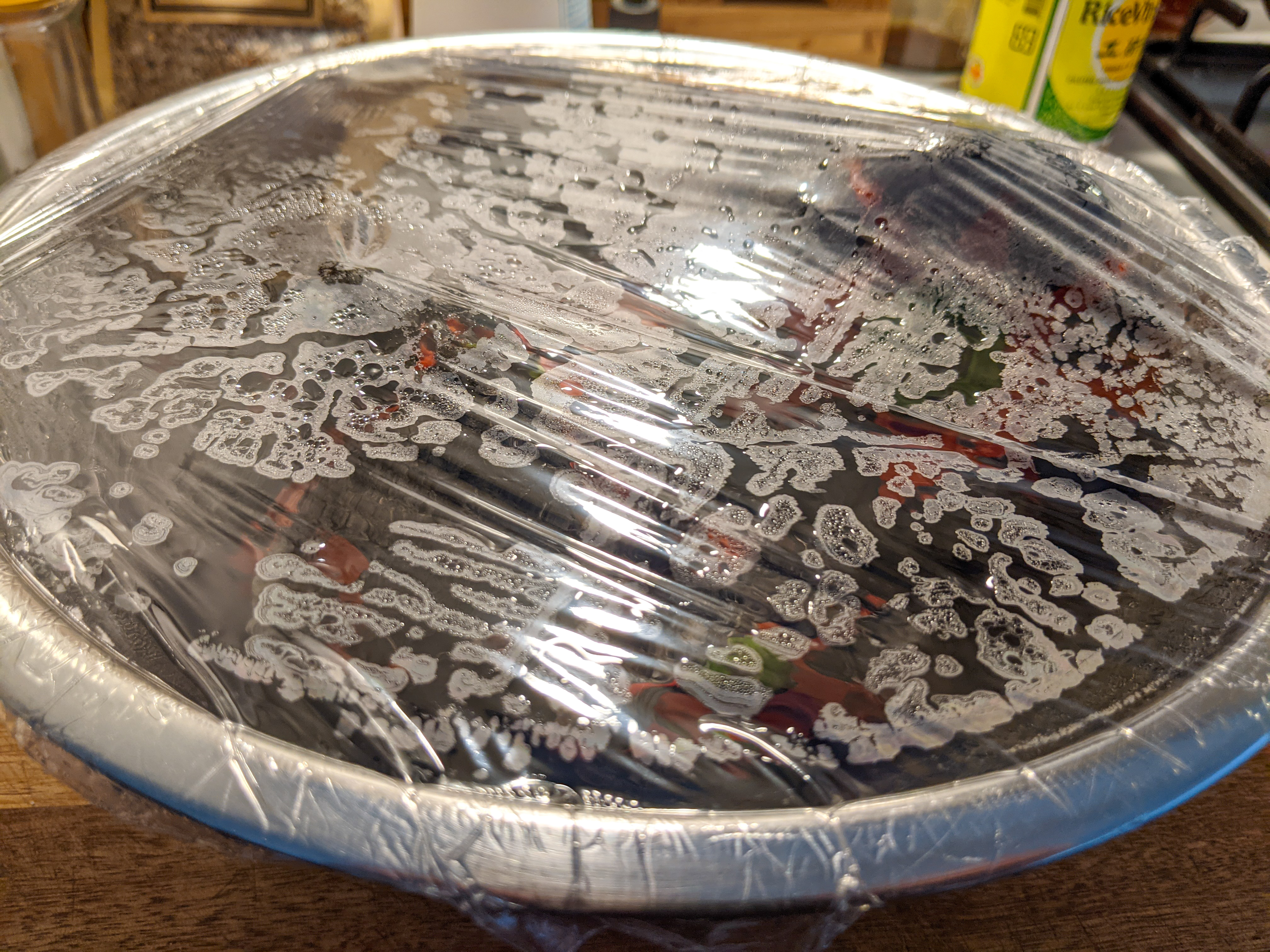 A metal bowl with blackened peppers in it. The surface is covered in plastic wrap