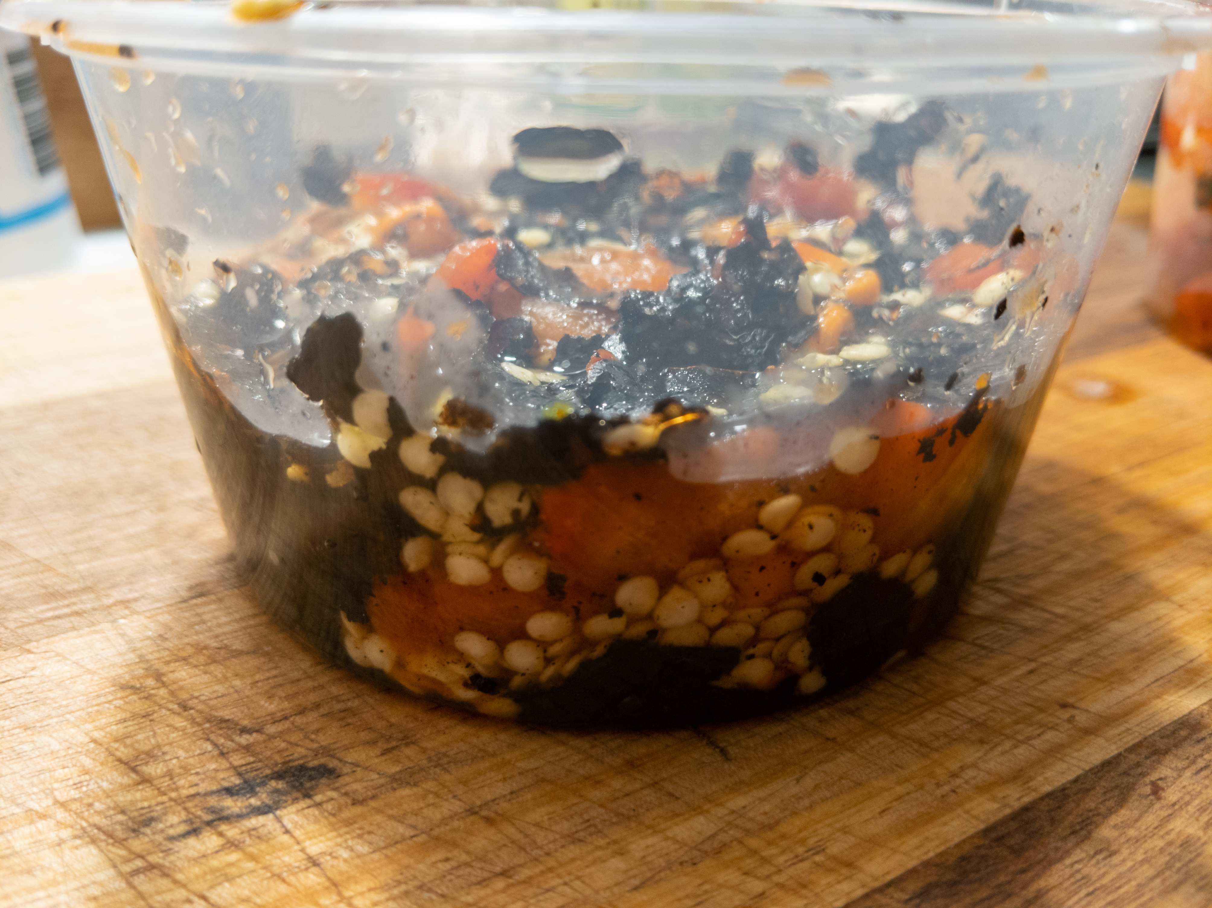 A plastic container filled with the pepper discard, with some liquid surrounding it