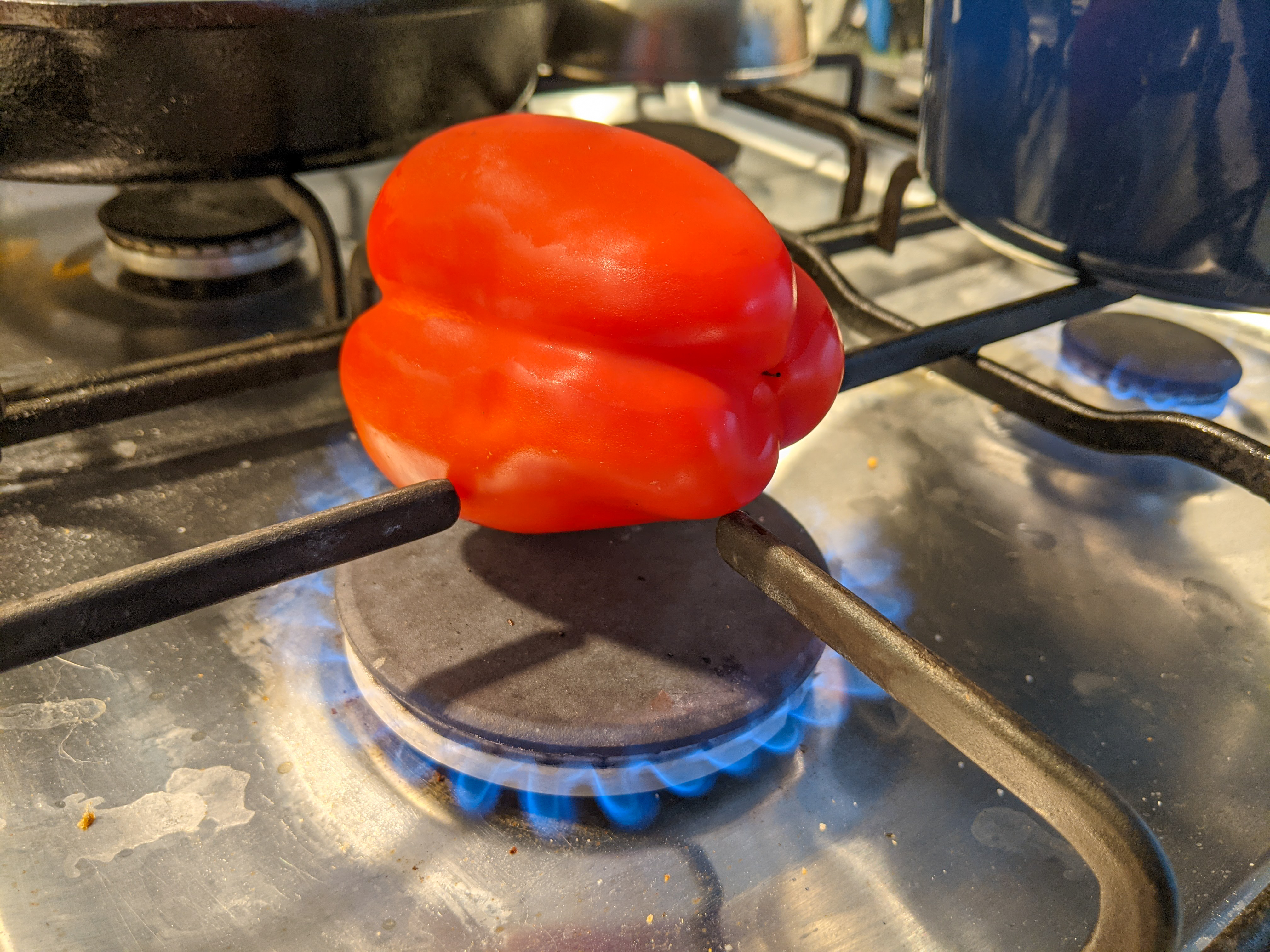 A red pepper sitting on the lit burner of a gas stove
