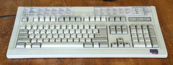 An image of a large, old keyboard. It has keyboard shortcuts for a program printed out and taped to the top of it