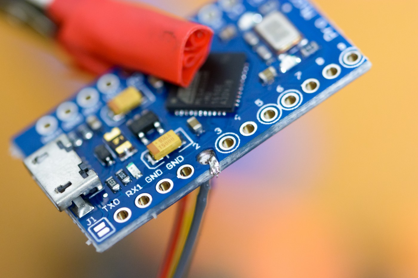 A macro image of a microcontroller with one of the wires from the previous image soldered to it via a through-hole.