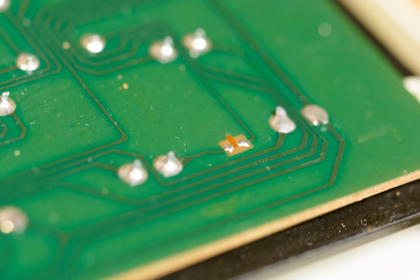 A macro image of a printed circuit board. There are many soldered component legs. In the middle is a small copper pad, with two disconnected blobs of solder.